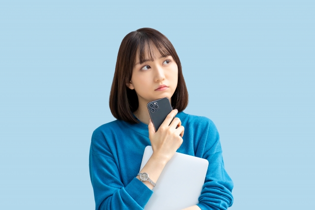 スマホを手に持ち悩んだ表情の女性の画像