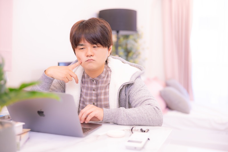 頬に指をあててPCを難しい表情で見ている男性の画像