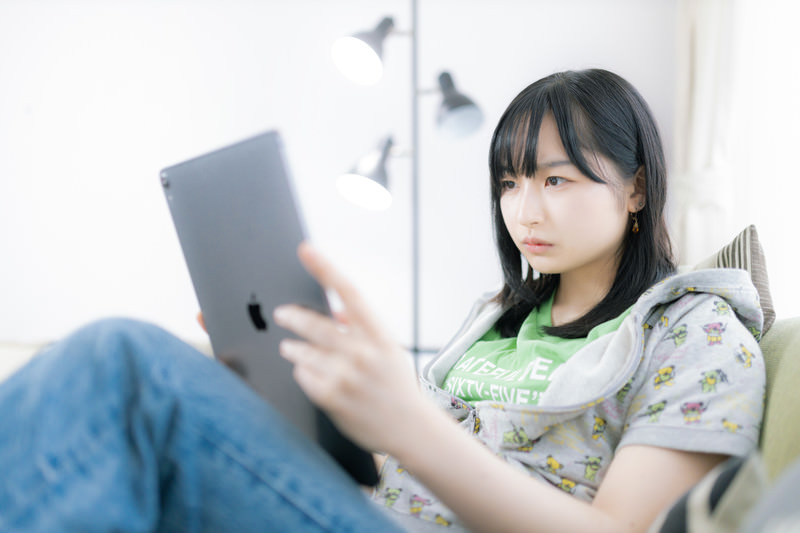 難しい表情でタブレットの画面を見つめる女性の画像