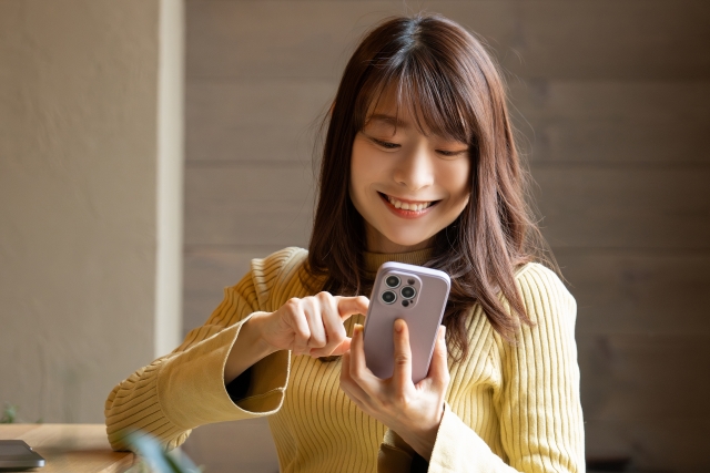 スマホを笑顔で操作する女性の画像