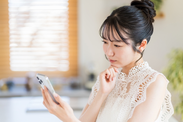 悩んだ表情でスマホの画面を見ている女性の画像