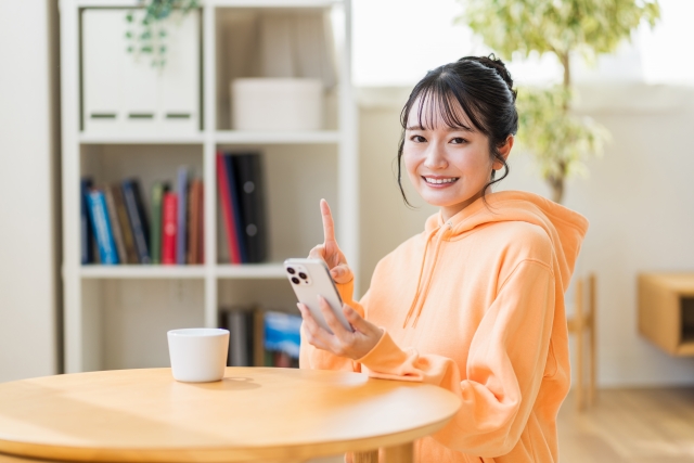 スマホを手に持ちカメラ目線で笑顔の女性の画像