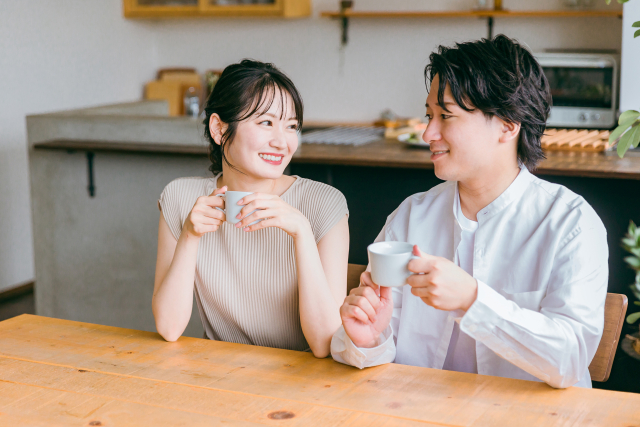 自宅でお茶を飲みながら楽しそうに会話をするカップルの画像