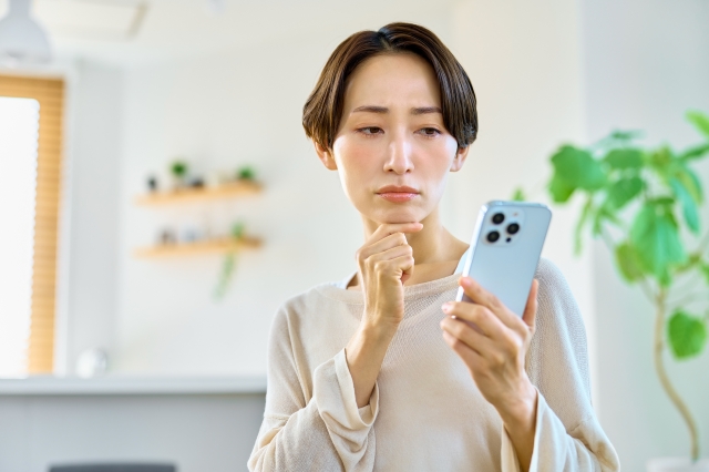 スマホを難しい表情で見つめている女性の画像