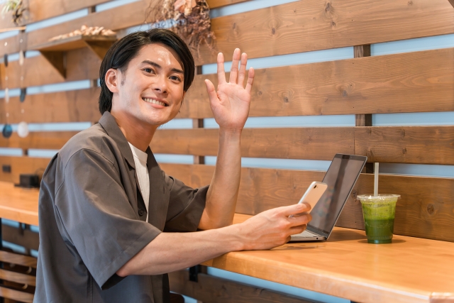 カフェで待ち合わせに現れたお相手に手を振る男性の画像