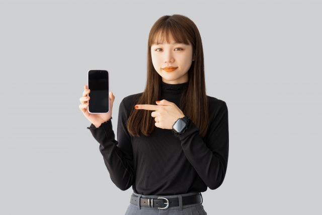 手に持ったスマホを指さしている女性の画像