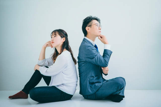 背中合わせに座って悩んでいる表情の男女の画像