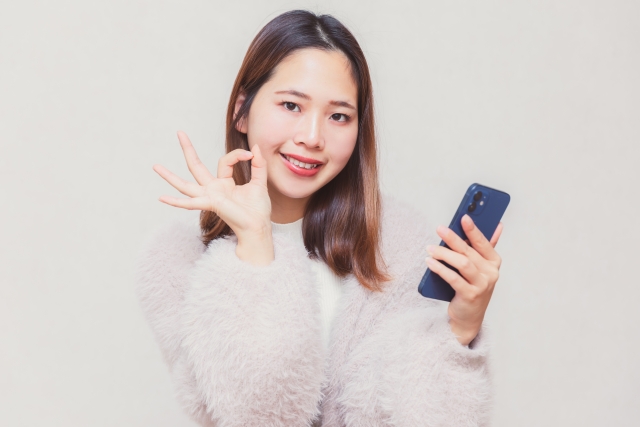 スマホを片手にOKサインをする女性の画像