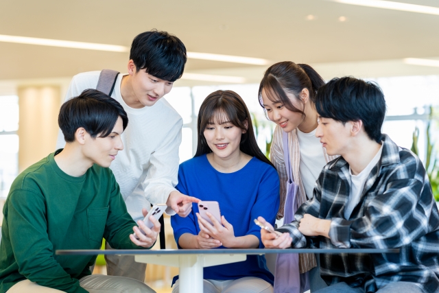 スマホを見ながらおしゃべりを楽しむ大学生グループの画像