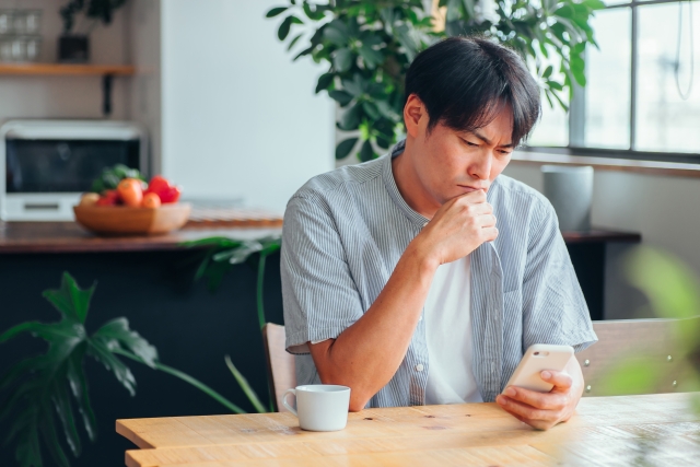 スマホを見ながら考え込んでいる男性