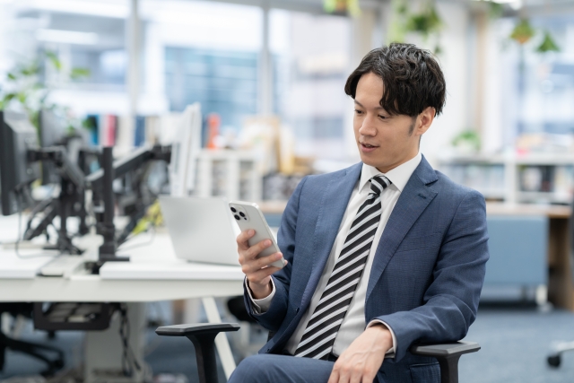 オフィスでスマホを見ている若い男性