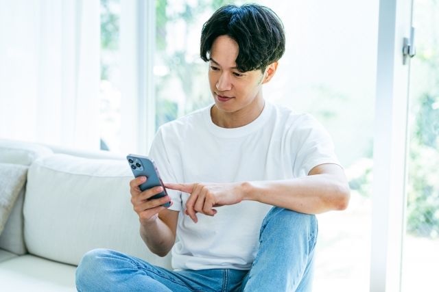 ソファに座ってスマホを操作する男性
