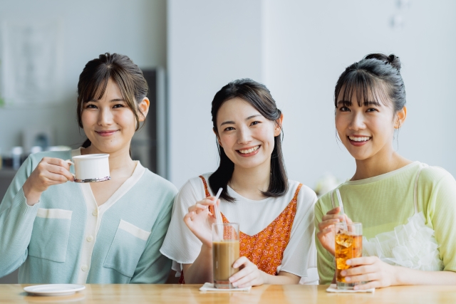 カフェで飲み物を手にカメラ目線で笑顔の3人の女性