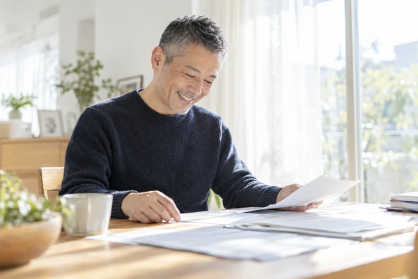 自宅のダイニングテーブルで、入会に出す書類がそろっているかを確かめている40代後半の男性
