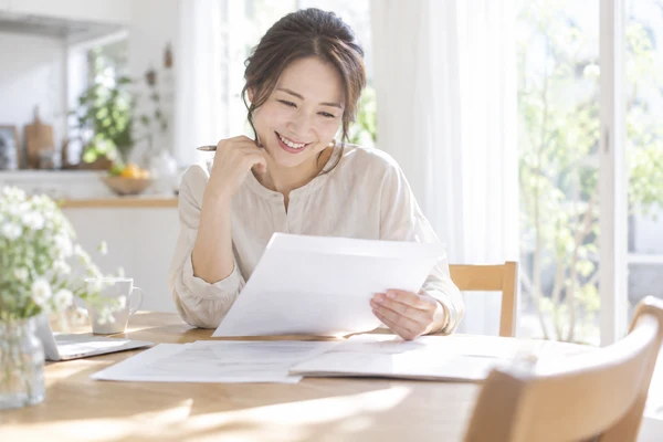 自宅のダイニングテーブルで、契約の書類を広げて内容を確かめている30代の女性