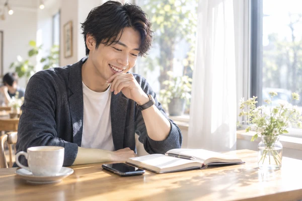 カフェの窓際で、婚活にかかる料金を見比べている20代の男性