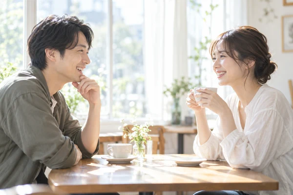 明るい窓辺のカフェの席で向かい合って話している30代の男女