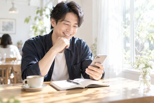 カフェの窓際で、結婚相談所の料金を見比べている30代の男性