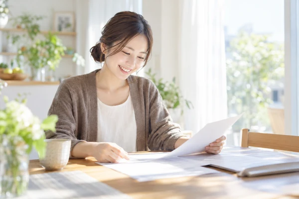 自宅のダイニングテーブルで、契約書面に書かれている条件を確かめている30代前半の女性
