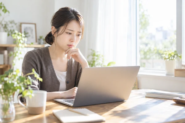 自宅の窓辺の机で、結婚相談所のページを見比べている30代前半の女性