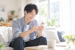 明るい窓辺のソファで、スマートフォンから婚活の予定を確かめている30代の男性