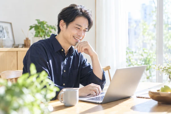 自宅のダイニングテーブルでノートパソコンを開き、お相手の検索条件を見直している30代後半の男性