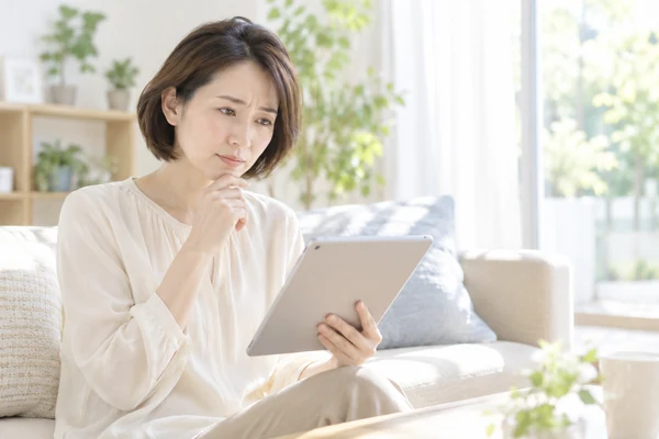 明るいリビングのソファで、タブレットで結婚相談所について調べている40代前半の女性