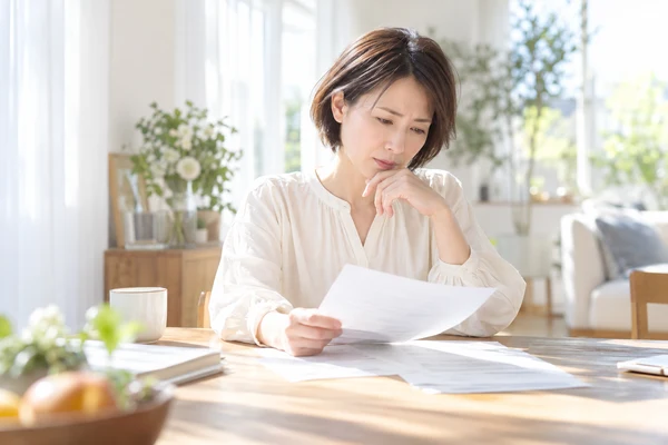 自宅のダイニングテーブルで契約書面を広げ、やめるときの条件を読んでいる40代前半の女性